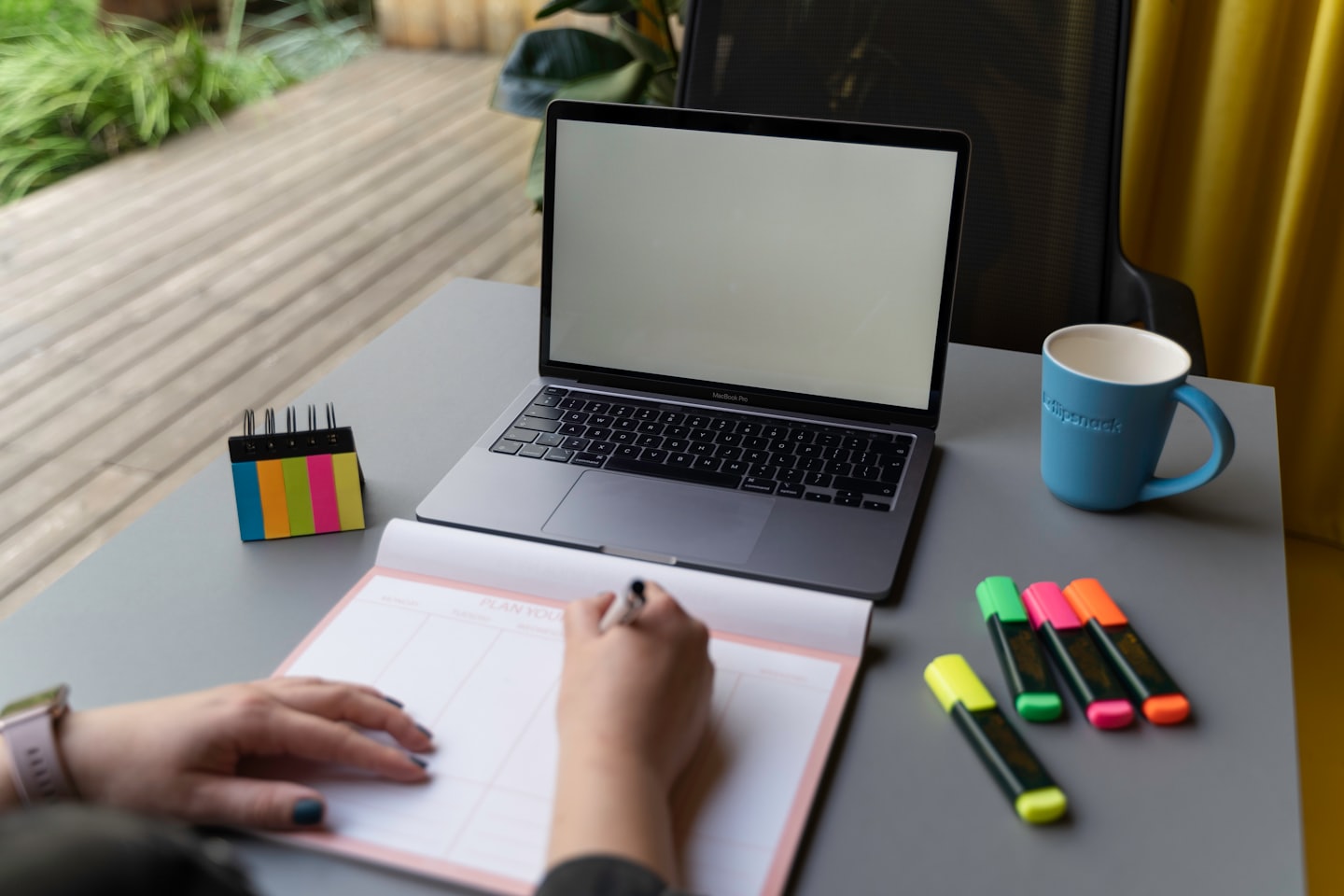Hands writing in a planner next to an open laptop.