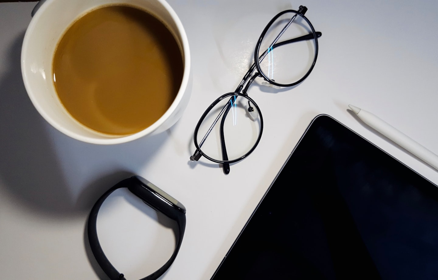 A desk with a coffee mug, glasses, smartwatch, and tablet.